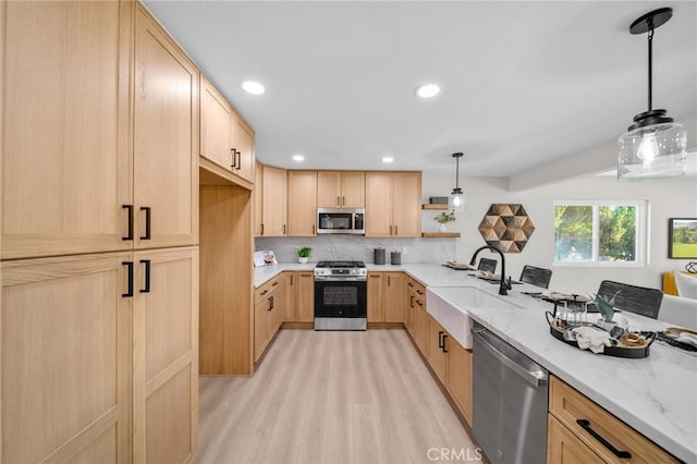 kitchen with stainless steel appliances, light brown cabinetry, light wood-style floors, a sink, and light stone counters