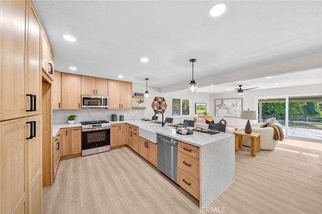 kitchen with stainless steel appliances, light brown cabinetry, a peninsula, a sink, and light wood-style floors
