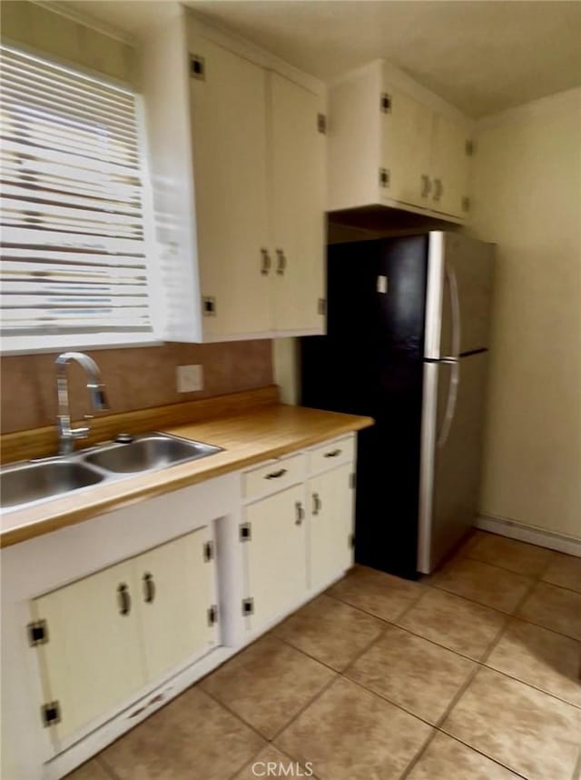kitchen featuring a sink, freestanding refrigerator, white cabinets, light countertops, and light tile patterned floors
