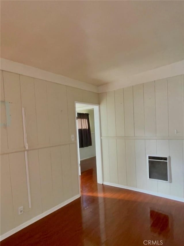 unfurnished room featuring wood finished floors, a decorative wall, heating unit, baseboards, and a fireplace