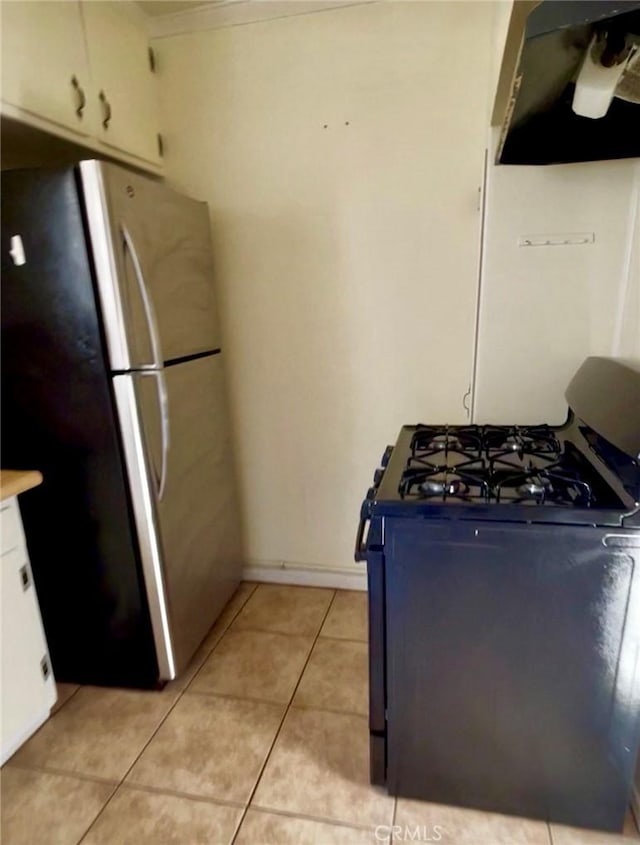 kitchen with range with gas stovetop, freestanding refrigerator, extractor fan, light tile patterned flooring, and white cabinetry