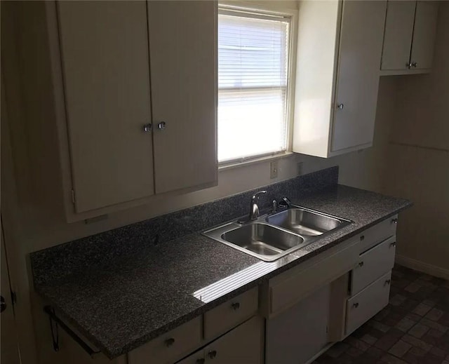 kitchen featuring a sink, white cabinets, dark countertops, and baseboards