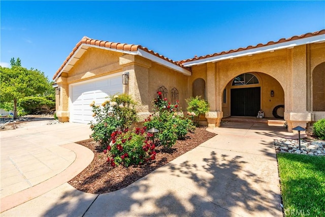 doorway to property with stucco siding, driveway, a garage, and a tiled roof