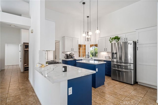 kitchen with stainless steel appliances, a towering ceiling, blue cabinets, a peninsula, and white cabinetry