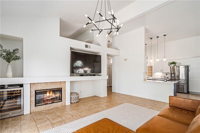 living area with beverage cooler, light tile patterned floors, a towering ceiling, a chandelier, and a tile fireplace