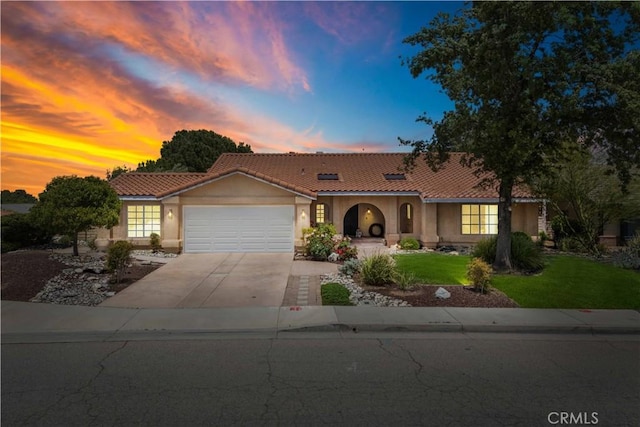 mediterranean / spanish home featuring stucco siding, a garage, a tile roof, and a yard