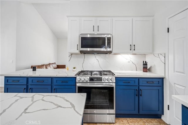 kitchen featuring appliances with stainless steel finishes, blue cabinets, backsplash, white cabinetry, and light stone countertops