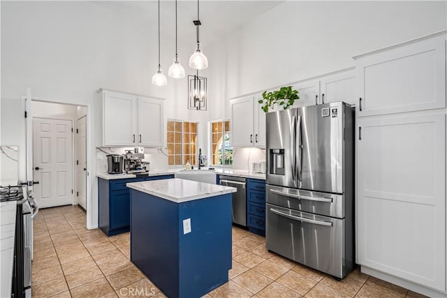 kitchen featuring stainless steel appliances, a towering ceiling, a sink, blue cabinetry, and light countertops