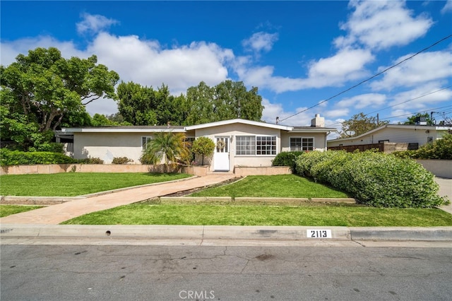 ranch-style home featuring a front yard, stucco siding, driveway, and a chimney