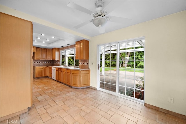 kitchen featuring light countertops, baseboards, white dishwasher, a tray ceiling, and a ceiling fan