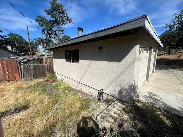 view of side of home featuring fence, stucco siding, and a garage