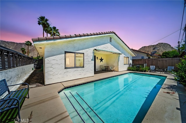 54415 Eisenhower Dr, La Quinta, CA 92253 - back of property at dusk with a patio area, a fenced backyard, stucco siding, and a tiled roof