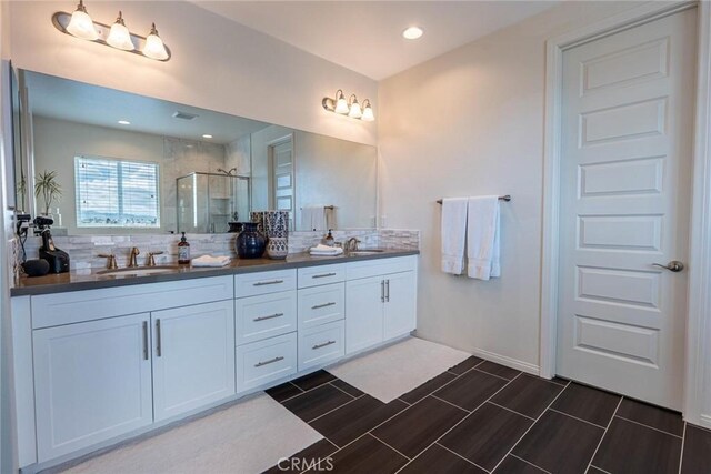 bathroom with decorative backsplash, a shower stall, double vanity, baseboards, and recessed lighting