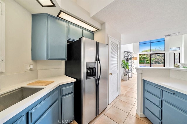 5145 Tortuga Dr Unit 209, Huntington Beach, CA 92649 - kitchen with stainless steel refrigerator with ice dispenser, light tile patterned floors, blue cabinetry, light countertops, and a textured ceiling