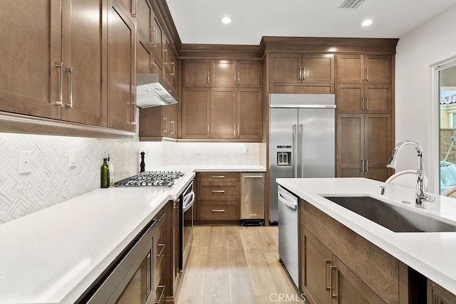 20702 W Chestnut Cir, Porter Ranch, CA 91326 - kitchen featuring under cabinet range hood, a sink, light wood-style floors, appliances with stainless steel finishes, and light countertops