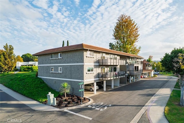 2134 Via Puerta Unit O, Laguna Woods, CA 92637 - view of home's exterior with covered and uncovered parking, a tiled roof, a balcony, and stucco siding
