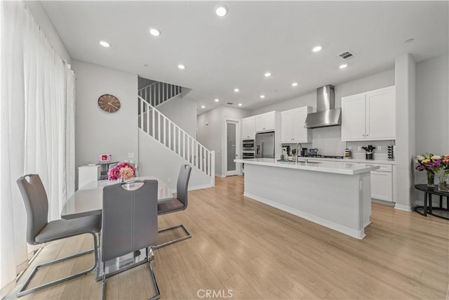 27218 Narrowleaf Willow Ln, Valencia, CA 91381 - kitchen featuring wall chimney range hood, stainless steel fridge with ice dispenser, white cabinetry, a kitchen island with sink, and light countertops