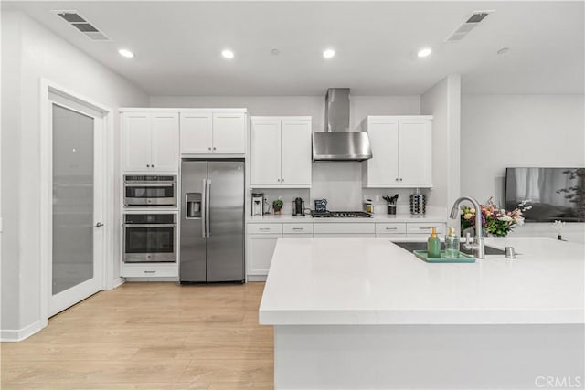 27218 Narrowleaf Willow Ln, Valencia, CA 91381 - kitchen with appliances with stainless steel finishes, wall chimney range hood, a sink, white cabinetry, and light countertops