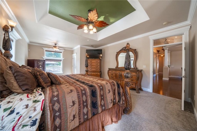 carpeted bedroom featuring a tray ceiling, decorative columns, a ceiling fan, and baseboards