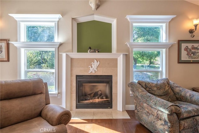 living area with a tiled fireplace, plenty of natural light, and wood finished floors