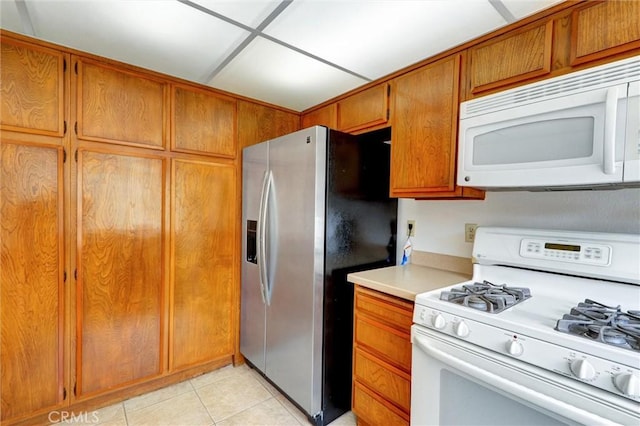11000 Woodruff Ave Unit 14, Downey, CA 90241 - kitchen with white appliances, light countertops, light tile patterned flooring, and brown cabinetry