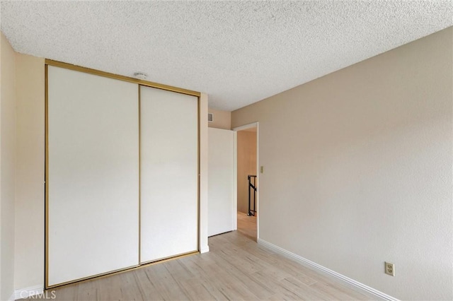 11000 Woodruff Ave Unit 14, Downey, CA 90241 - unfurnished bedroom with a textured ceiling, light wood finished floors, a closet, and baseboards