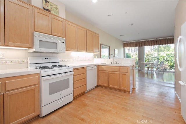 kitchen with white appliances, light brown cabinetry, a peninsula, a sink, and light wood-style flooring