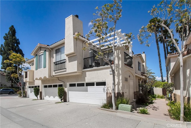 view of front of house with a chimney, a balcony, an attached garage, concrete driveway, and stucco siding