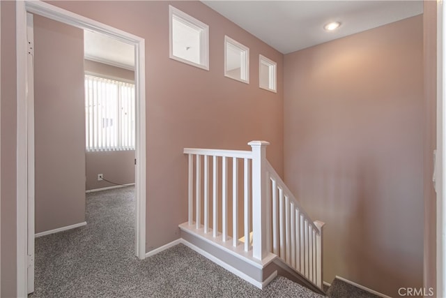 hall with an upstairs landing, carpet flooring, and baseboards