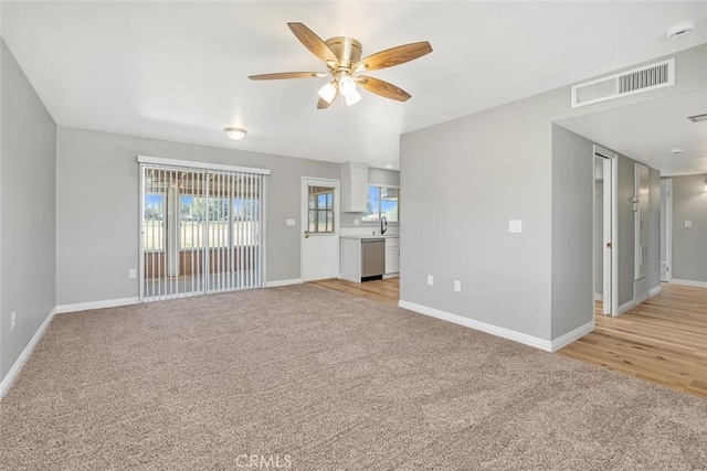 unfurnished living room with a ceiling fan, light colored carpet, baseboards, and a sink