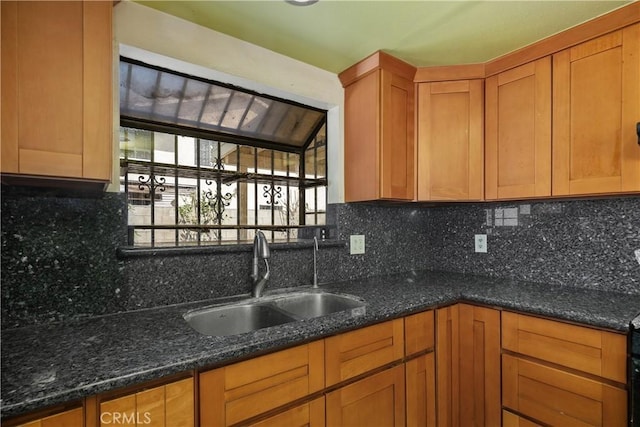 kitchen with a sink, decorative backsplash, dark stone countertops, and brown cabinets