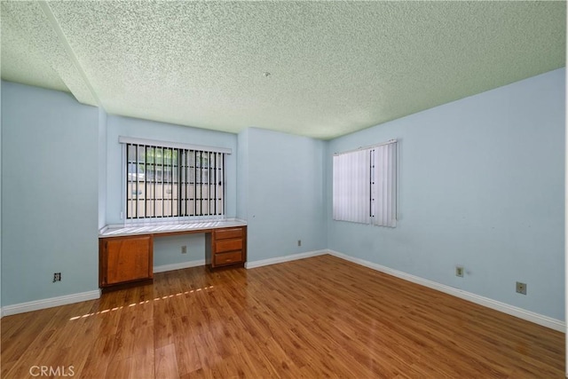 spare room with a textured ceiling, wood finished floors, and baseboards