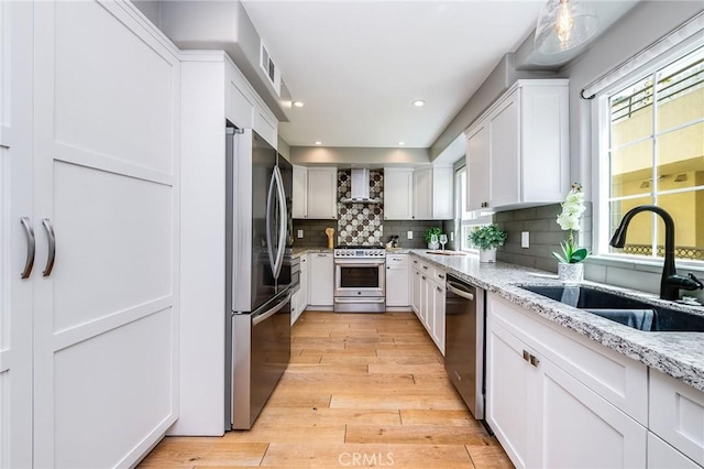 kitchen with appliances with stainless steel finishes, a sink, backsplash, white cabinets, and light wood-type flooring