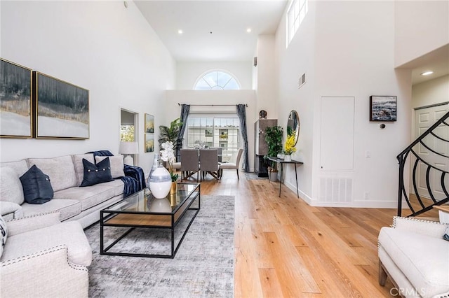 living room with a towering ceiling, stairs, light wood-style flooring, and baseboards