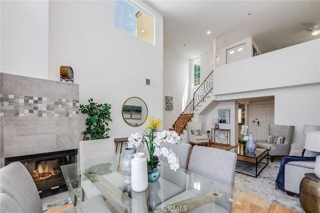 living room featuring a high ceiling, stairs, wood finished floors, a tiled fireplace, and ceiling fan
