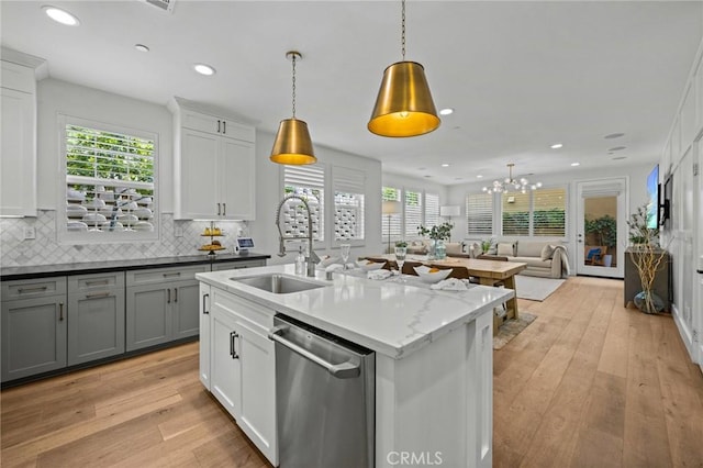 kitchen with stainless steel dishwasher, a sink, light wood-style floors, open floor plan, and tasteful backsplash
