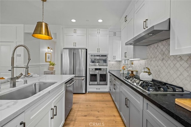 kitchen featuring appliances with stainless steel finishes, under cabinet range hood, a sink, white cabinetry, and hanging light fixtures