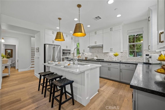 kitchen with a sink, tasteful backsplash, appliances with stainless steel finishes, a kitchen bar, and pendant lighting