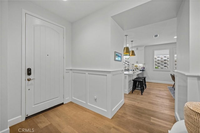 entryway with light wood-style floors, a wainscoted wall, and a decorative wall