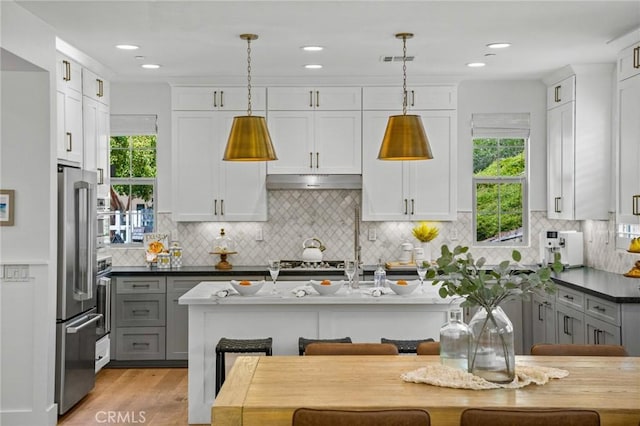 kitchen featuring high end fridge, under cabinet range hood, white cabinets, pendant lighting, and recessed lighting