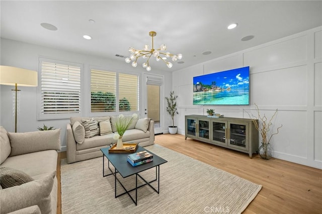 living area with a chandelier, a decorative wall, wood finished floors, and recessed lighting