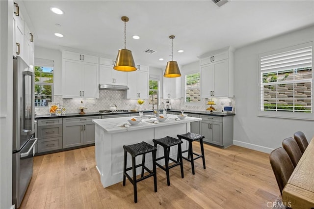 kitchen with high end fridge, decorative backsplash, a breakfast bar area, gray cabinets, and recessed lighting