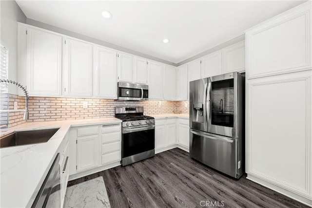 kitchen featuring stainless steel appliances, a sink, light stone countertops, white cabinetry, and recessed lighting