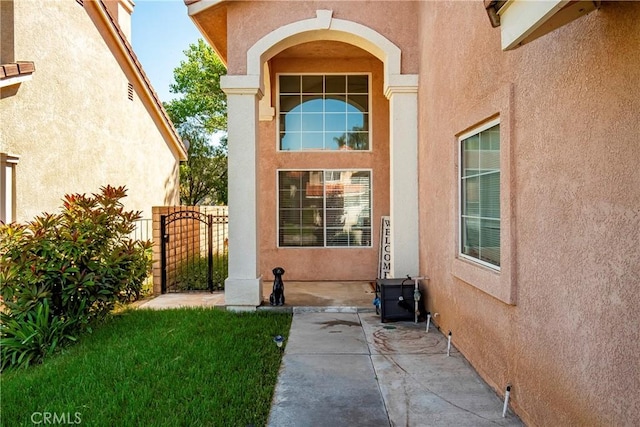 view of exterior entry featuring stucco siding, a gate, and a patio
