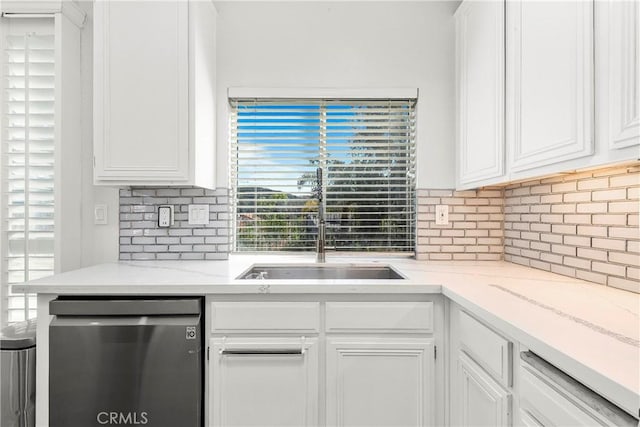 kitchen featuring stainless steel dishwasher, a sink, white cabinets, and decorative backsplash