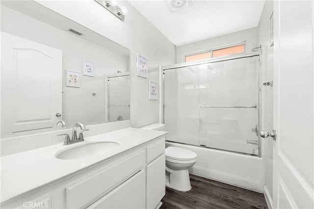 full bath with wood finished floors, toilet, vanity, and combined bath / shower with glass door