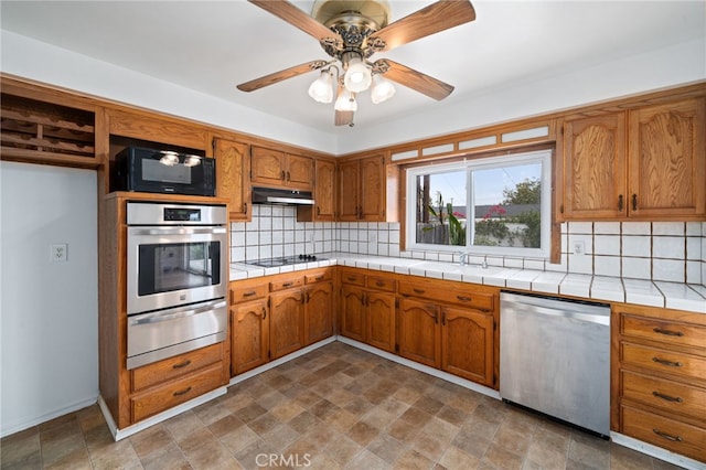 15408 Mottley Dr, La Mirada, CA 90638 - kitchen with stainless steel appliances, a warming drawer, under cabinet range hood, brown cabinets, and tasteful backsplash