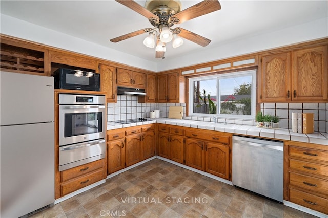 15408 Mottley Dr, La Mirada, CA 90638 - kitchen with appliances with stainless steel finishes, a warming drawer, under cabinet range hood, and brown cabinetry