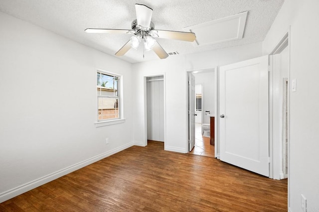unfurnished bedroom with wood finished floors, a textured ceiling, baseboards, ceiling fan, and ensuite bathroom