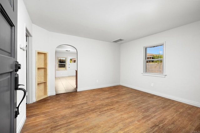 empty room with light wood finished floors, healthy amount of natural light, and arched walkways